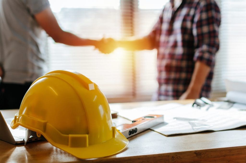 a contractor shaking hands with a person in the background with a hard hat in the foreground